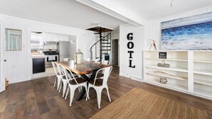 A spacious kitchen with white cabinetry, a wooden dining table, and a view of the living area. - Sleeps 8-Cozy 3-Bedroom Cottage, 2 Blocks from the Strip, 10 Minutes from Spire (Geneva)