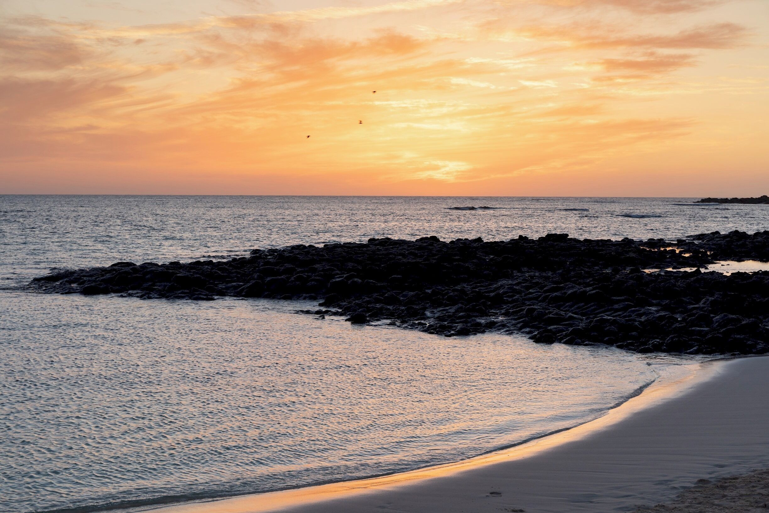A beach with a rocky shoreline and a sunset.