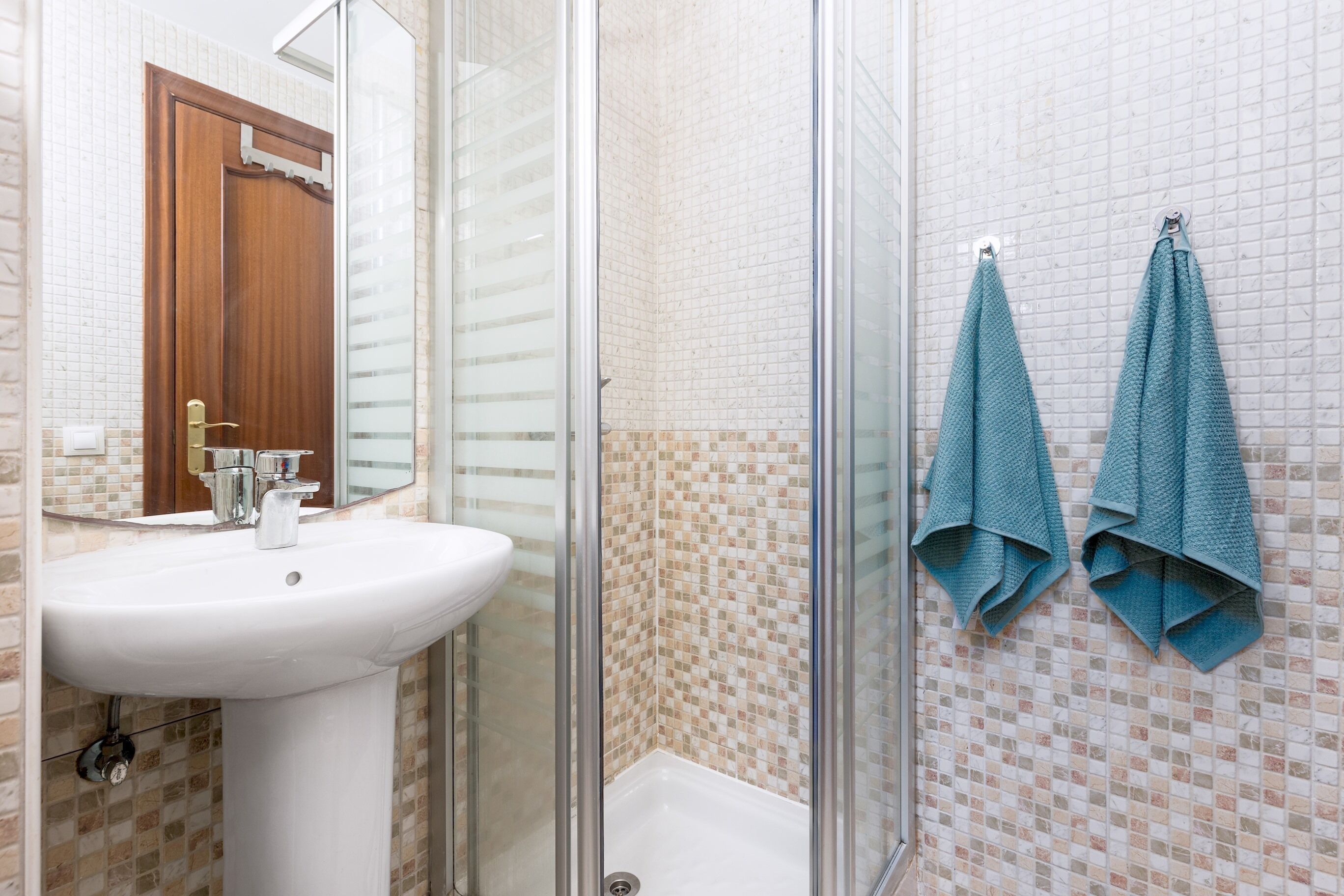 A bathroom with a white sink, a glass shower enclosure, and two towels hanging on the wall.