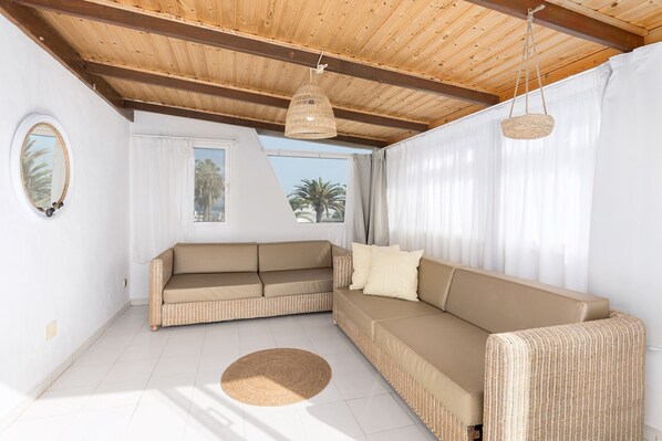 A room with a beige sofa, a round woven rug, and a hanging wicker light fixture.