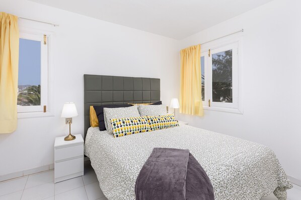 Un dormitorio con cama, mesitas de noche y cortinas.