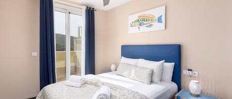 Een hotelkamer met een bed, nachtkastje, plafondventilator, raam met gordijnen en een kunstwerk aan de muur.