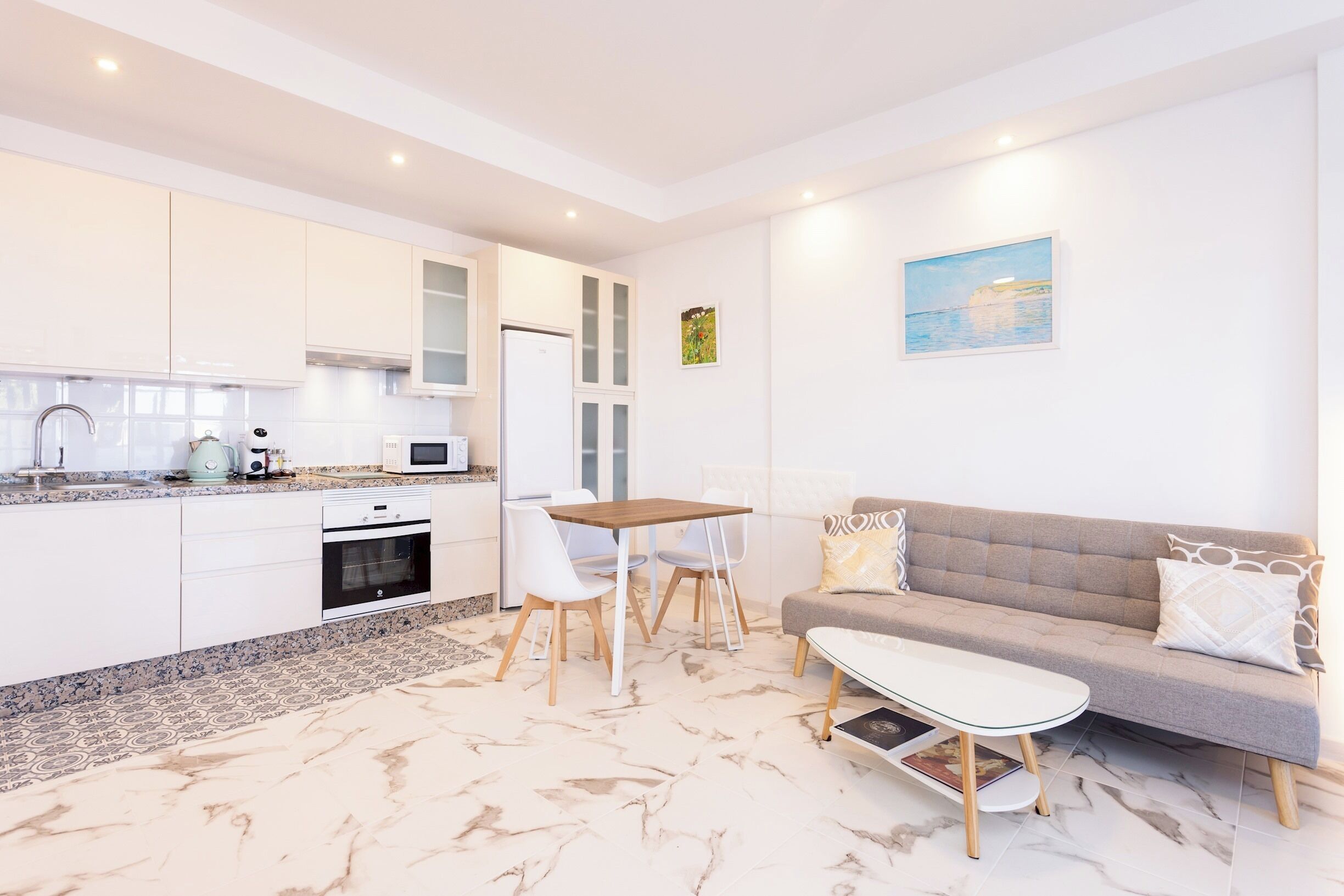 Una cucina moderna con mobili bianchi, un'area pranzo con tavolo e sedie, e un divano grigio con cuscini decorati.