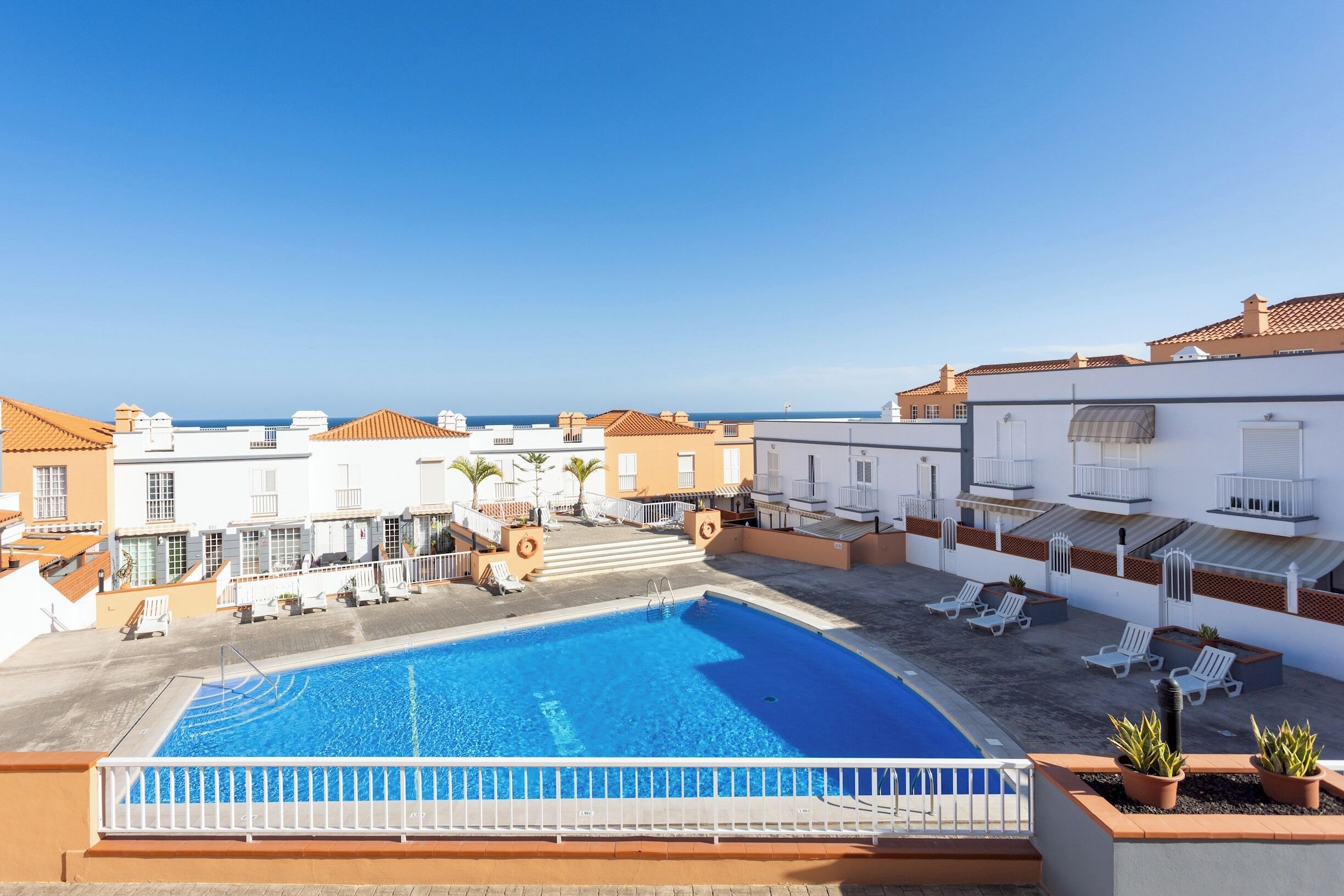 A rooftop swimming pool with a clear view of the sea, surrounded by white buildings with red-tiled roofs.