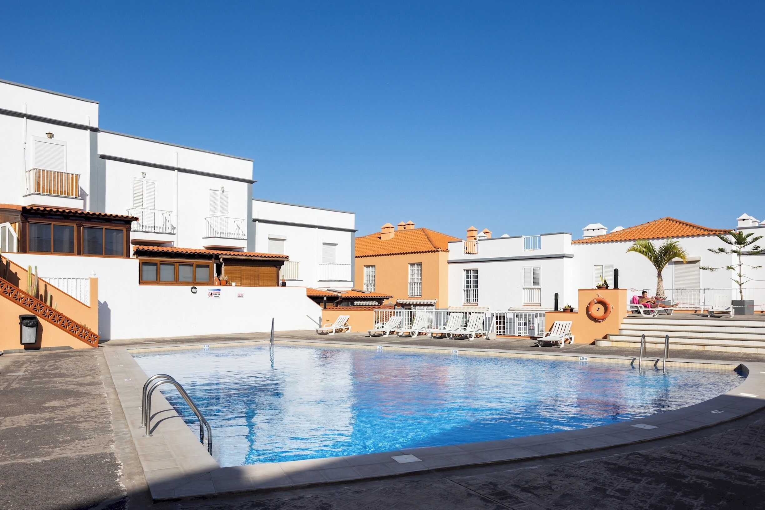 Ein Schwimmbecken mit Liegestühlen und wolkenlosem, blauem Himmel.