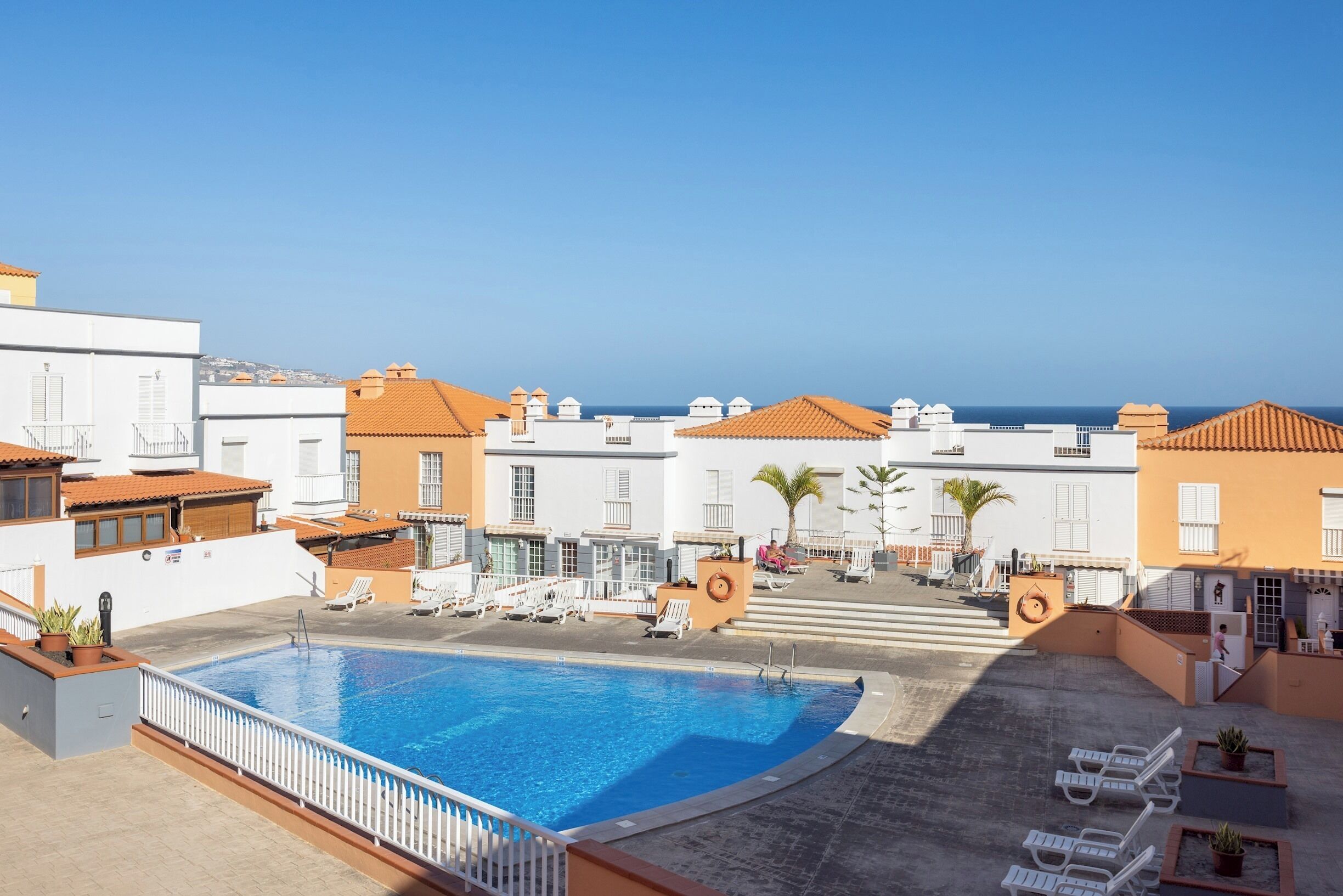 A rooftop pool area with lounge chairs, a swimming pool, and buildings with orange-tiled roofs.
