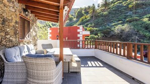 A covered outdoor seating area with wicker furniture and a stone wall. - Home2Book Valley Views  & Private Terrace Hermigua (Hermigua)