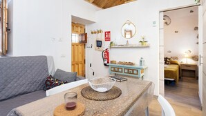 A cozy room with a wooden ceiling, a sofa, a table with a woven placemat, a small shelf with decorative items, and a bed with a yellow blanket. - Home2Book Valley Views  & Private Terrace Hermigua (Hermigua)