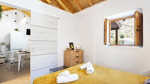 Een slaapkamer met een houten plafond, een bed met opgerolde handdoeken, een houten dressoir en een raam met open luik.