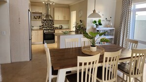 Eine geräumige Küche mit Holzausstattung, einer zentralen Kochinsel und einem Essbereich mit Holztisch und weißen Stühlen.