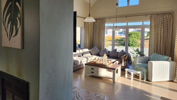Ein geräumiges Wohnzimmer mit Sofa, Sessel und Couchtisch, großen Fenstern und Deckenventilator.
