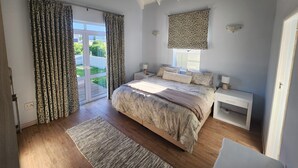 Ein Schlafzimmer mit einem Bett, Nachttischen, einem Fenster mit gemusterten Vorhängen und Blick auf Grünfläche.