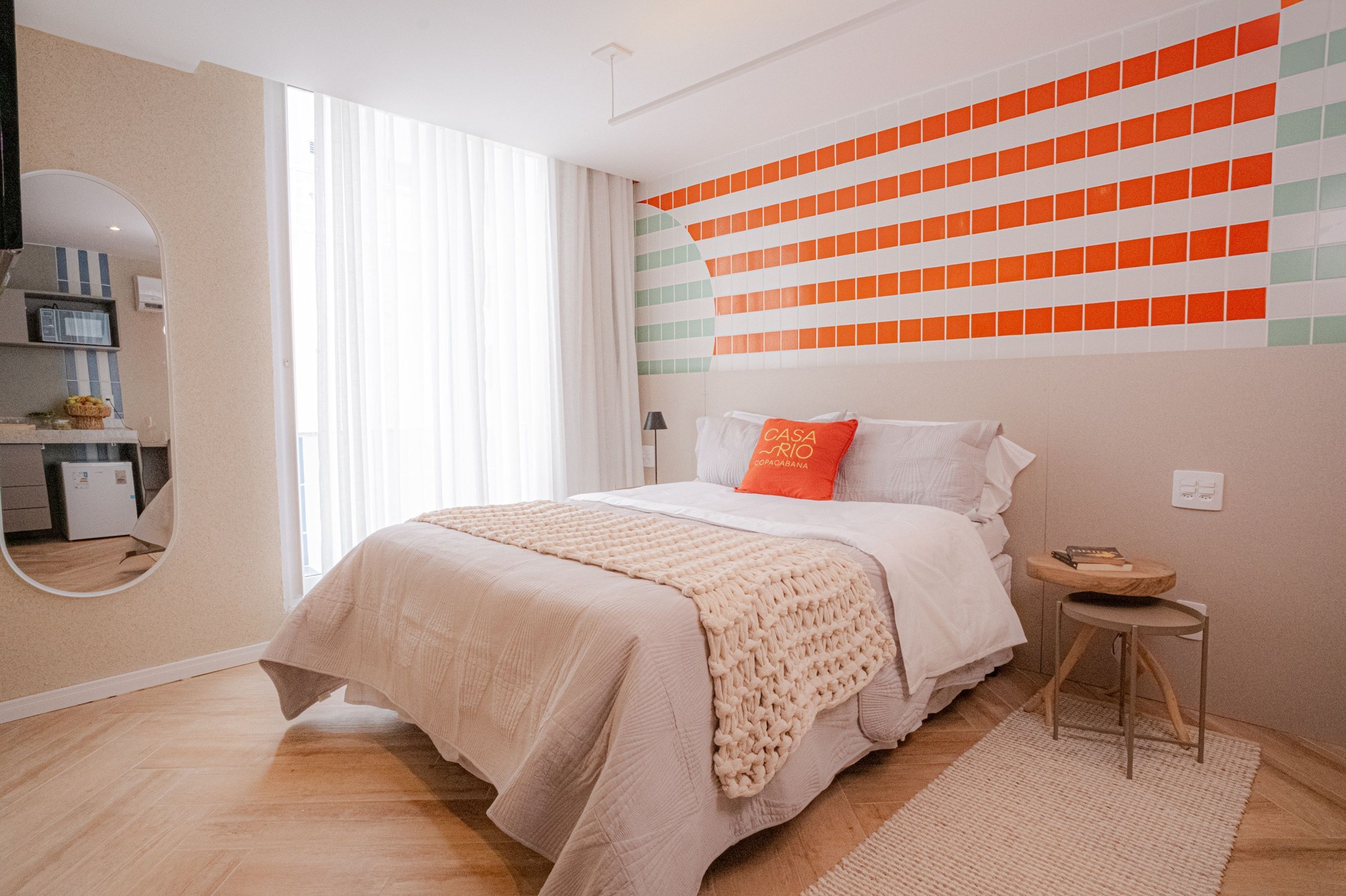 A bedroom with a bed, a bedside table, a mirror, and a wall with a geometric pattern.