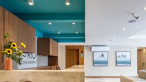 A modern reception area with a wooden reception desk, a vase with sunflowers, and framed artwork on the walls. - Refuge a few Steps From Copacabana Beach Q15 (Rio de Janeiro)