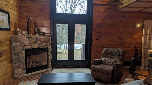 A cozy cabin interior with a stone fireplace, leather furniture, and a view of the outdoors through a large door. - Trego River House  (Trego)