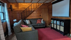 A cozy living room with a grey sofa, a red carpet, a bookshelf, and a staircase. - Trego River House  (Trego)