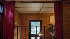 A wooden cabin interior with a balcony, a staircase, and a view of the outdoors. - Trego River House  (Trego)