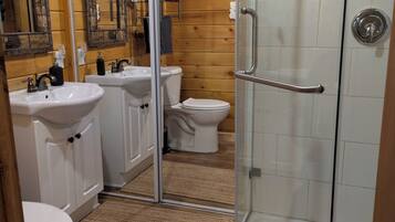 A bathroom with wooden walls, a glass shower enclosure, a white sink, and a toilet.