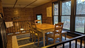 A wooden cabin interior with a dining table and chairs, a large window, and a view of trees. - Trego River House  (Trego)