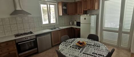 Een moderne keuken met houten kastjes, een gasfornuis en een ingebouwde oven. Er staat een eettafel met een rond tafelkleed waarop stadsnamen staan.