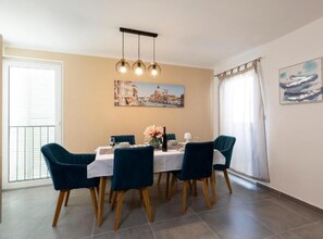 A dining area with a table set for four, a chandelier, a cityscape painting, and a window with curtains.