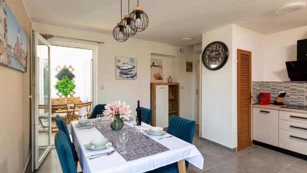 A dining area with a table set for four, a kitchen with modern appliances, and a door leading to another room.