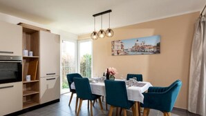 A dining area with a table set for four, a kitchen with a built-in oven, and a cityscape painting on the wall.