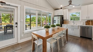 Una cocina moderna con armarios blancos, una mesa de comedor de madera y un amplio ventanal con vistas a una terraza.