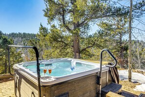 A hot tub with a glass of wine and a glass of champagne, surrounded by trees and a wooden deck. - Private Fishing Pond: Mtn-View Home in Florissant! (Florissant)
