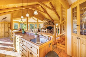 A wooden cabin interior with a kitchen area featuring a large island with a sink, wooden cabinets, and a stone fireplace. - Private Fishing Pond: Mtn-View Home in Florissant! (Florissant)