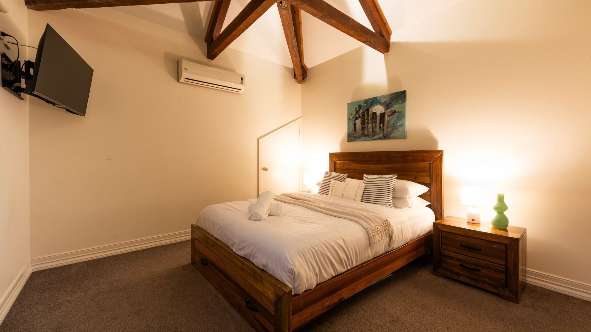 Un dormitorio con una cama de madera, una mesita de noche, un cuadro y un aire acondicionado.
