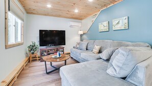 A living room with a grey sofa, a wooden coffee table, a flat-screen TV, and a staircase leading to an upper floor.
