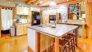 A kitchen with wooden cabinets, a central island with stools, a refrigerator, and a microwave. - 11 Mi to Olympic NP: Port Angeles Retreat w/ Deck (Port Angeles)