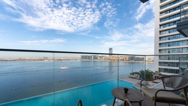 A balcony with a view of a large body of water, a pool, and a cityscape in the background. - Premium 2BR Emaar Beachfront w/ Beach Access (Dubai)