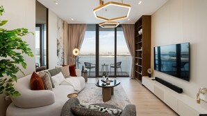 A modern living room with a sofa, coffee table, and a flat-screen TV. There is a large window with a view of the sea. - Premium 2BR Emaar Beachfront w/ Beach Access (Dubai)