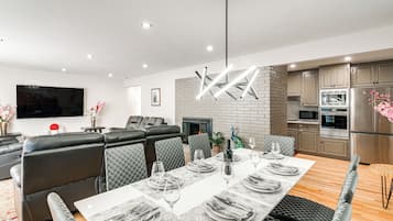 A modern living room with a dining area, a fireplace, and a kitchen with stainless steel appliances.