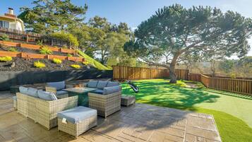 A patio with wicker furniture and a small table, surrounded by a well-maintained lawn and a wooden fence.
