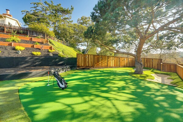 A backyard with a green artificial turf, a wooden fence, and a tree. - 2 Mi to Beach: Home w/ Patio in Del Rey Oaks! (Del Rey Oaks)