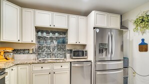 A kitchen with white cabinets, a stainless steel refrigerator, a microwave, and a dishwasher. - Stylish St Pete Studio: Full Kitchen & Laundry (St. Petersburg)