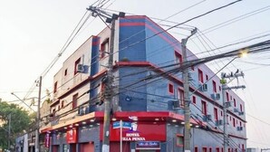 Un hotel de varios pisos con fachada roja y azul, múltiples unidades de aire acondicionado y una entrada visible.