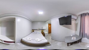 Una habitación de hotel moderna con una cama curvada, un televisor de pantalla plana, una mesita y una zona de ducha.
