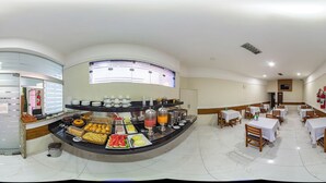Un bufé de desayuno con diversas opciones de comida y una estación de café. Hay mesas y sillas dispuestas para comer.