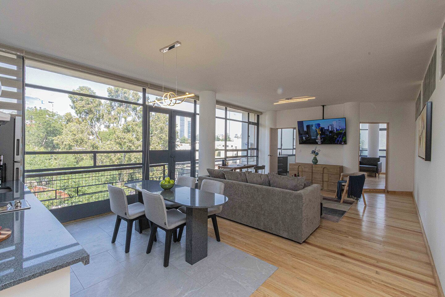 A modern living room with a dining area, large windows, and a flat-screen TV.