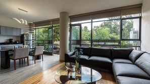Un espacio habitable moderno con una mesa de centro de vidrio, un sofá de cuero negro y vistas a zonas verdes a través de amplios ventanales.