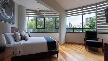 Un dormitorio moderno con una cama grande, una silla y vistas de la ciudad a través de amplios ventanales.
