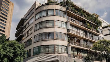 Un hotel de varios pisos con fachada curva, área de estar al aire libre con sombrillas y vista a la calle.