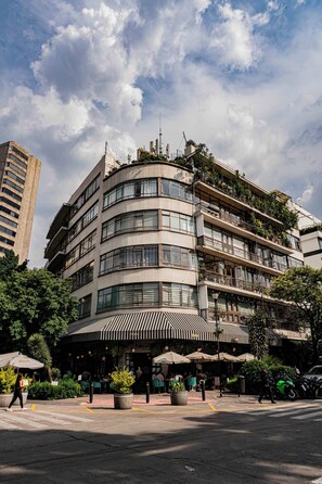 Un hotel de varios pisos con fachada curva, área de estar al aire libre con sombrillas y vista a la calle.