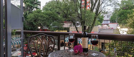 Un balcon avec une table et des chaises en métal, une bouteille de vin et un verre de vin rouge.
