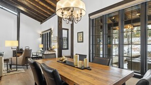 A dining area with a wooden table, black chairs, and a chandelier. There are windows with a view of the outdoors. - Luxury home near Mt Rushmore!  King beds in 3 of 4 bedrooms!  (Keystone)
