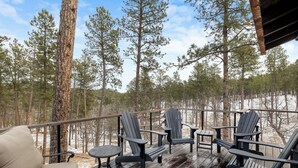 A wooden deck with Adirondack chairs and a sofa, overlooking a forested area with snow on the ground. - Luxury home near Mt Rushmore!  King beds in 3 of 4 bedrooms!  (Keystone)